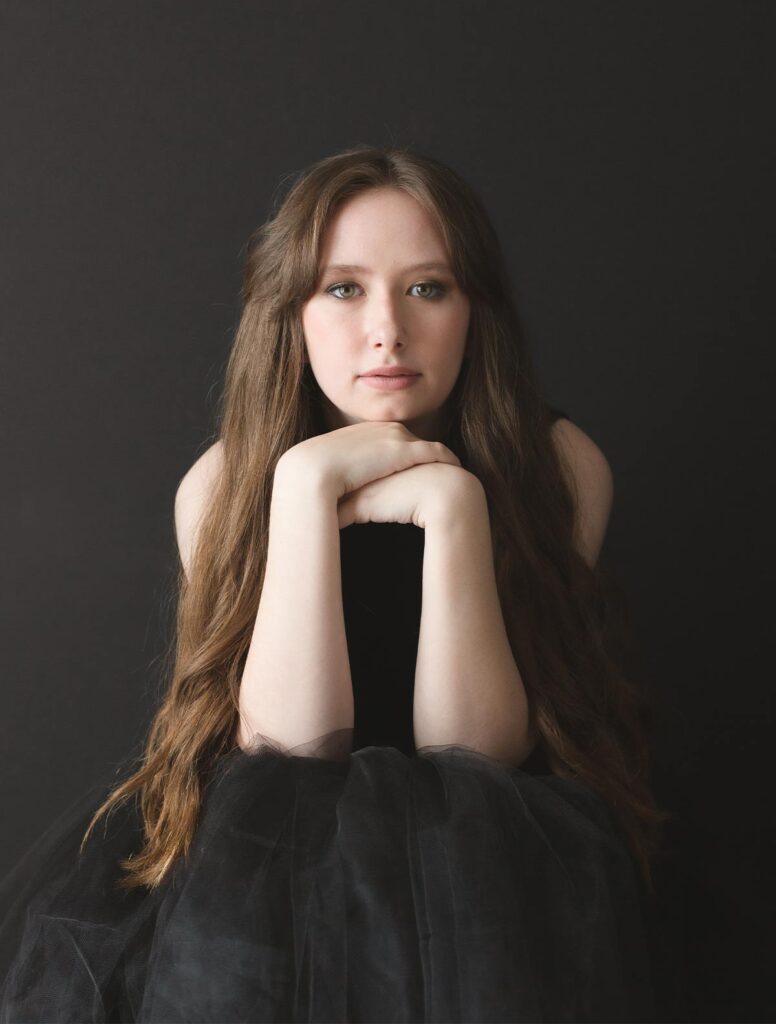 Teen in black tulle skirt poses with hands tucked under chin