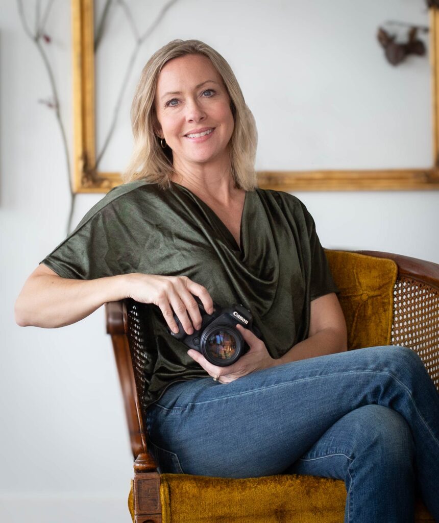 woman sits relaxed in a chair, holding a camera in her hands