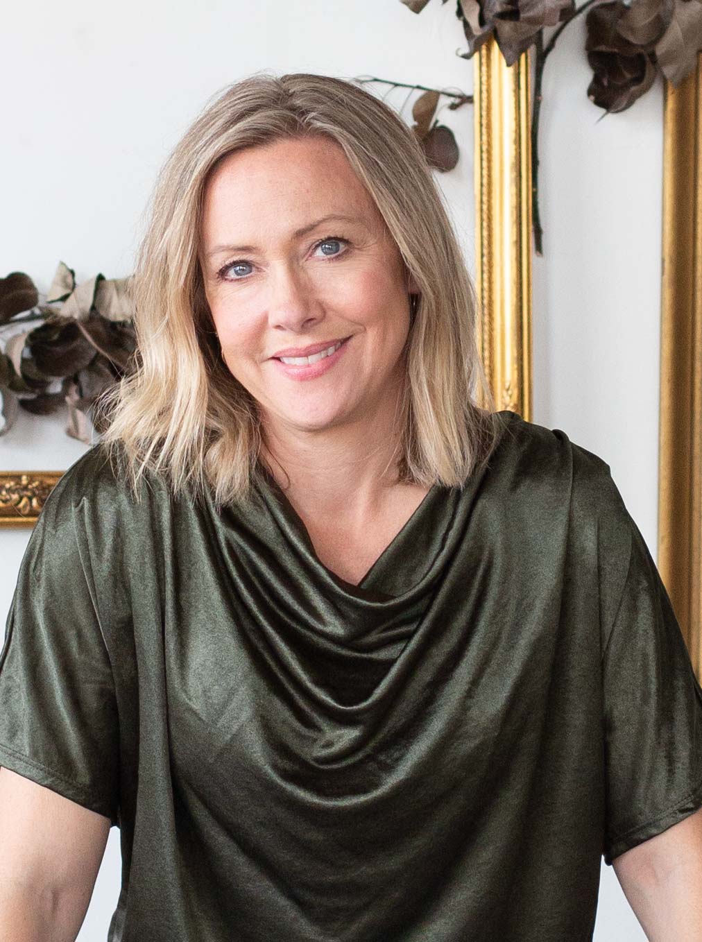 Woman smiles at camera. She is wearing a green top and has blonde hair