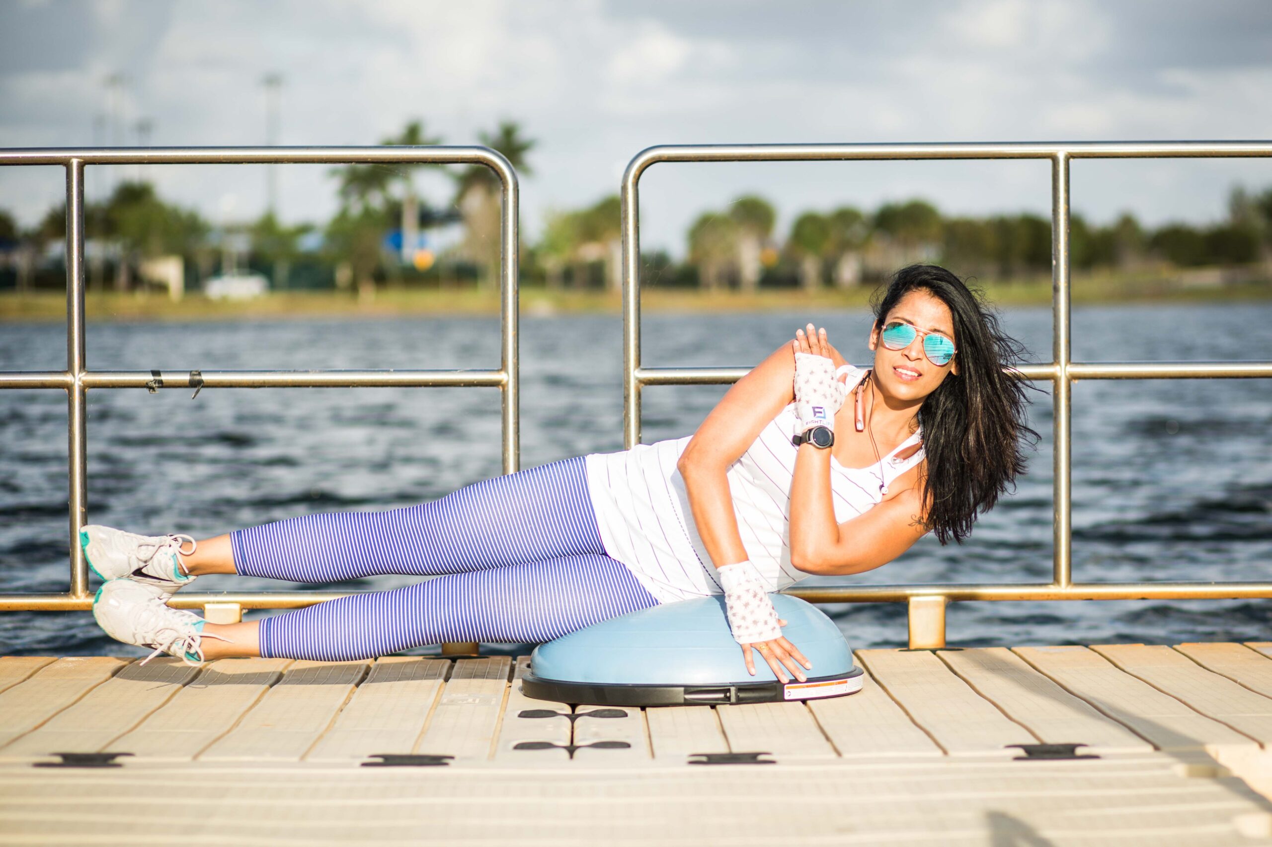 Woman exercises on exercise ball on a dock in front of a lake in the sun
