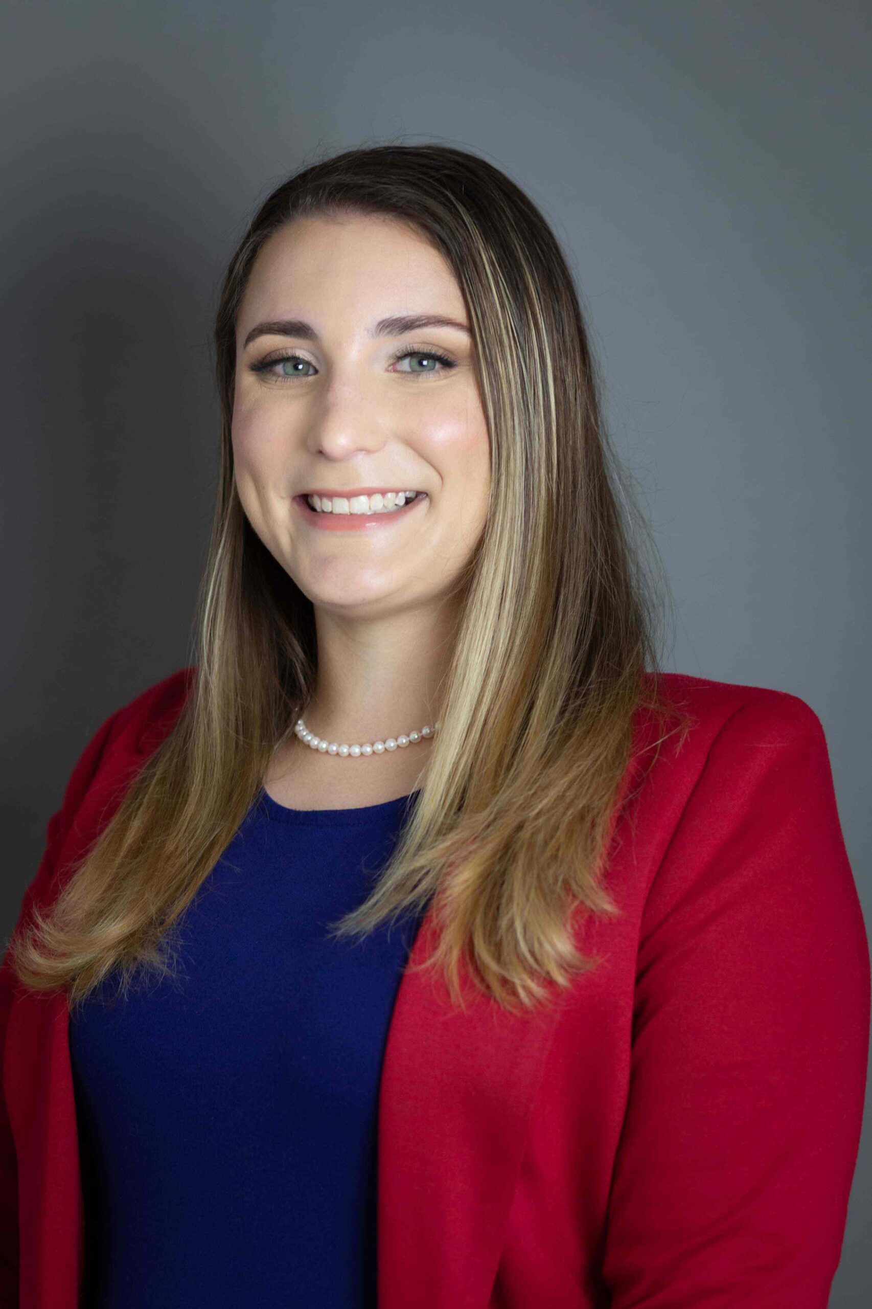 Woman in blue dress and red cardigan smiles for a headshot